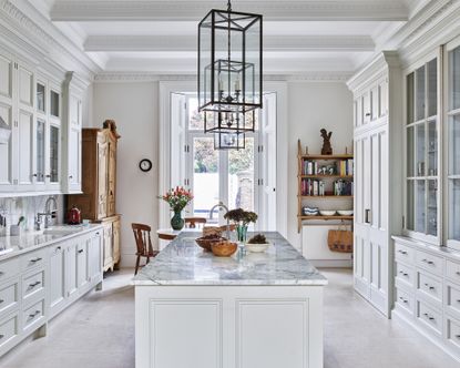 A kitchen with white cabinets and a marble topped island, with natural stone floor tiles