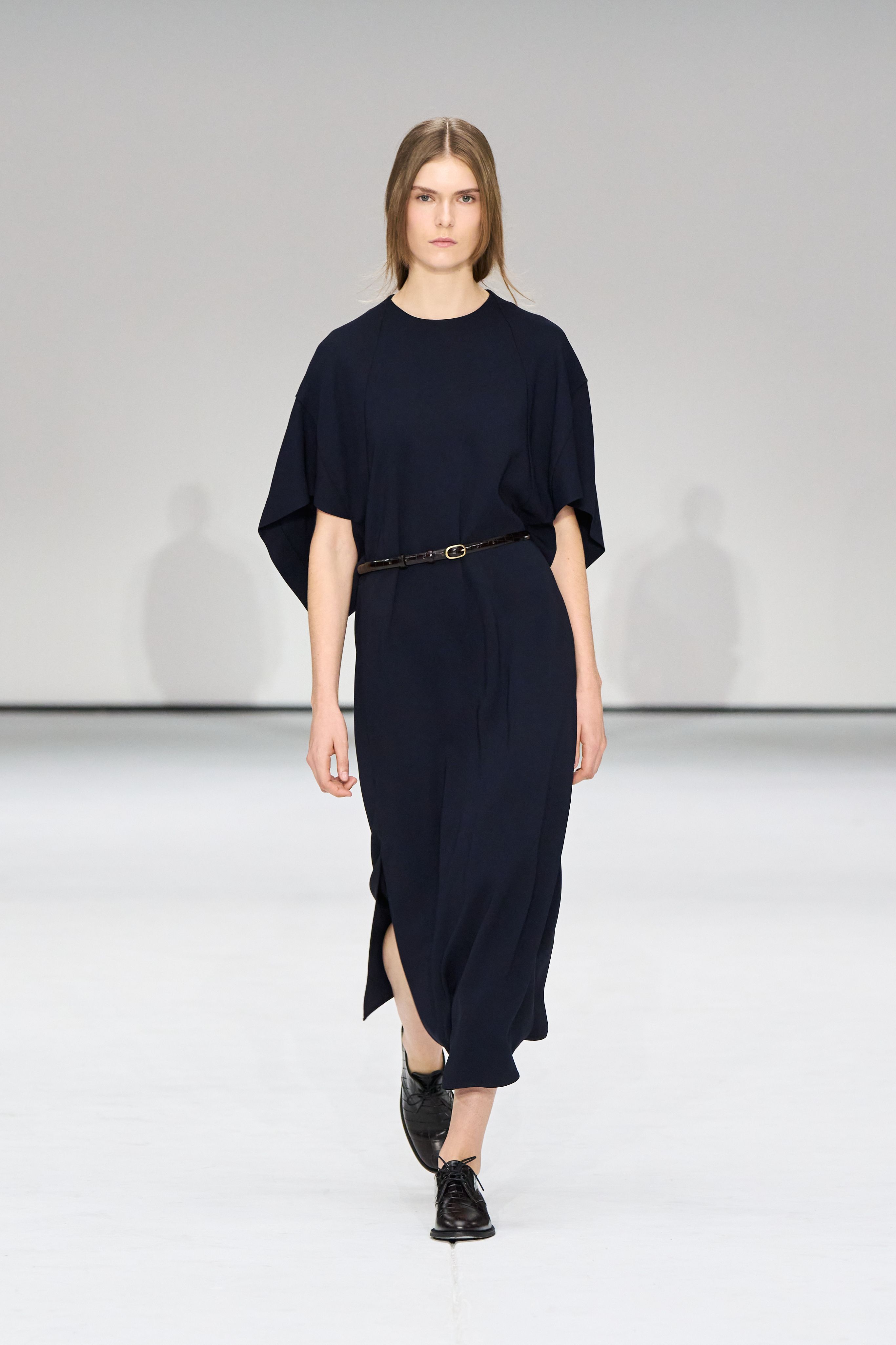 A woman wears a navy maxi dress with a black belt and derby shoes.