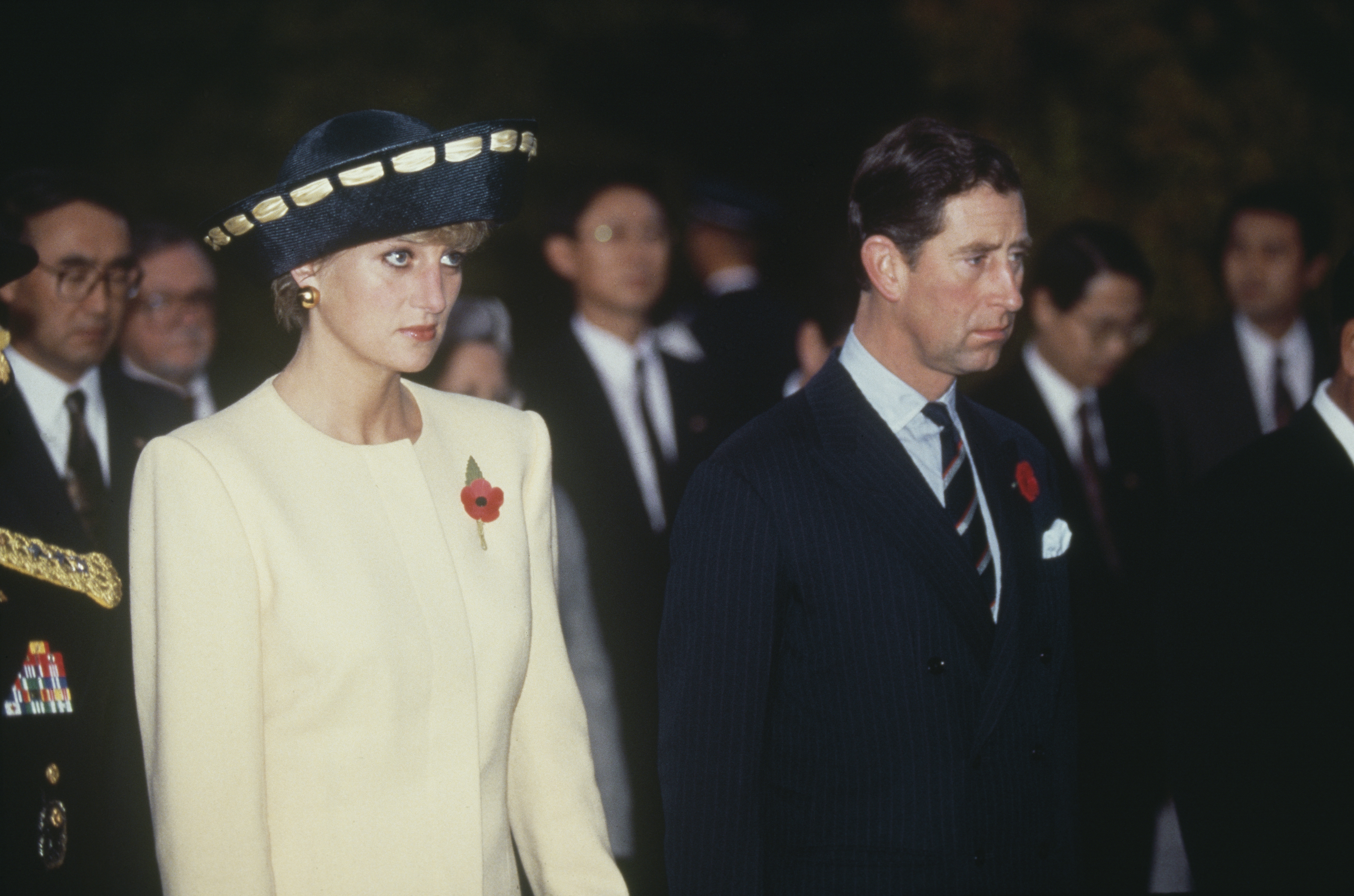 Diana wearing a yellow suit and black hat standing next to Prince Charles