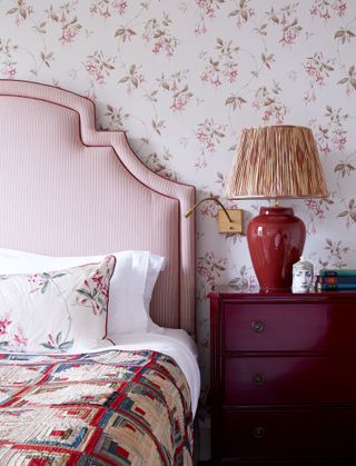 bedroom with red stripe headboard, red chest of drawers, red lamp, wallpaper with red petals, vintage throw