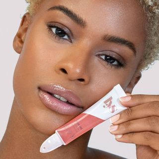 A model holding the Lys Beauty Glossy Lip Treatment Oil up to her face while wearing it on her lips, for Black-owned beauty and skincare brands.