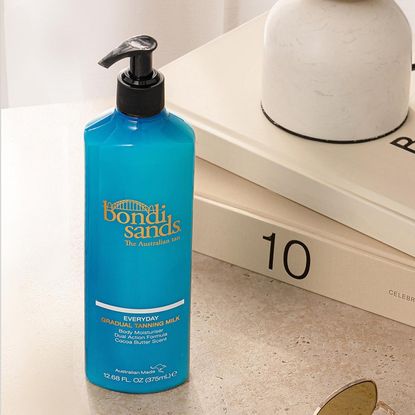 bottle of bondi sands Everyday Gradual Tanning Milk Body Moisturizer on beige table with books 