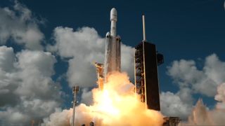 A white, triple-booster rocket launches into a blue sky.