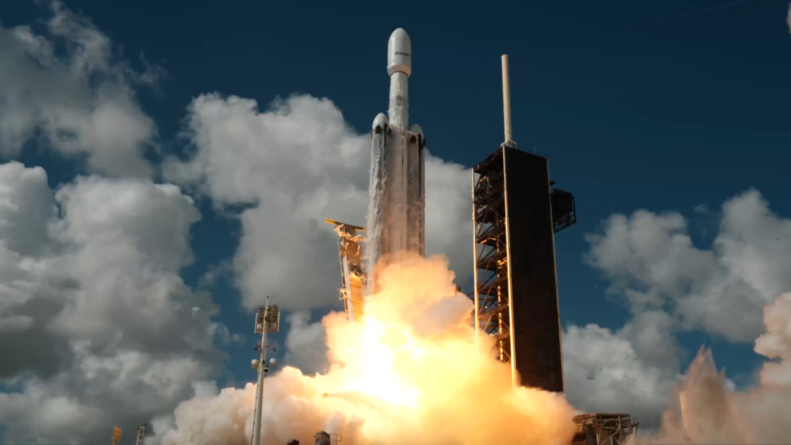 A white, triple-booster rocket launches into a blue sky.