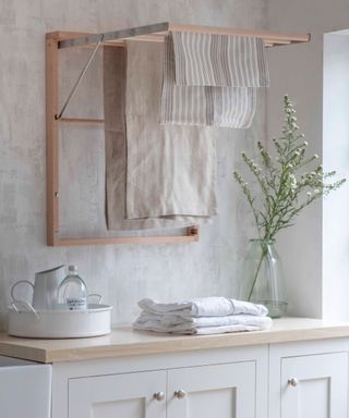 wooden and metal wall mounted drying rack open in utility room with wooden worktops and white cupboards
