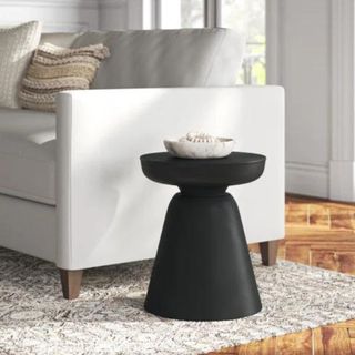 A black sculptural side table next to a white couch