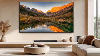The new Samsung QN90F, a 115-inch Neo QLED TV, wall mounted in a neutrally decorated room with a big window and neutral colored furniture