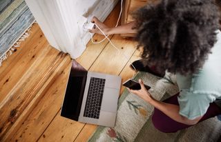 High angle view of young woman plugging mobile phone charger in electrical outlet at home