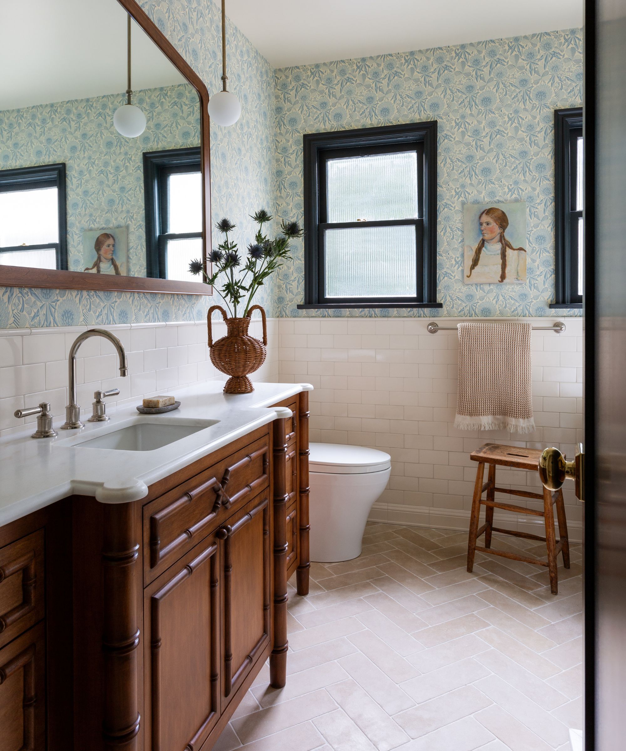 a blue and white floral wallpapered family bathroom with half heigh tile and a striking wooden antique bamboo style wooden vanity