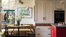 A vase of flowers on a circular kitchen table against white cabinets and white walls.