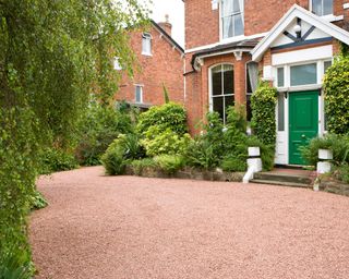 front garden of a large detached house with red gravel driveway and holly bushes