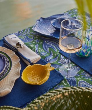 A closeup of a blue and green outdoor dining table with a wine glass and small fish-shaped bowl