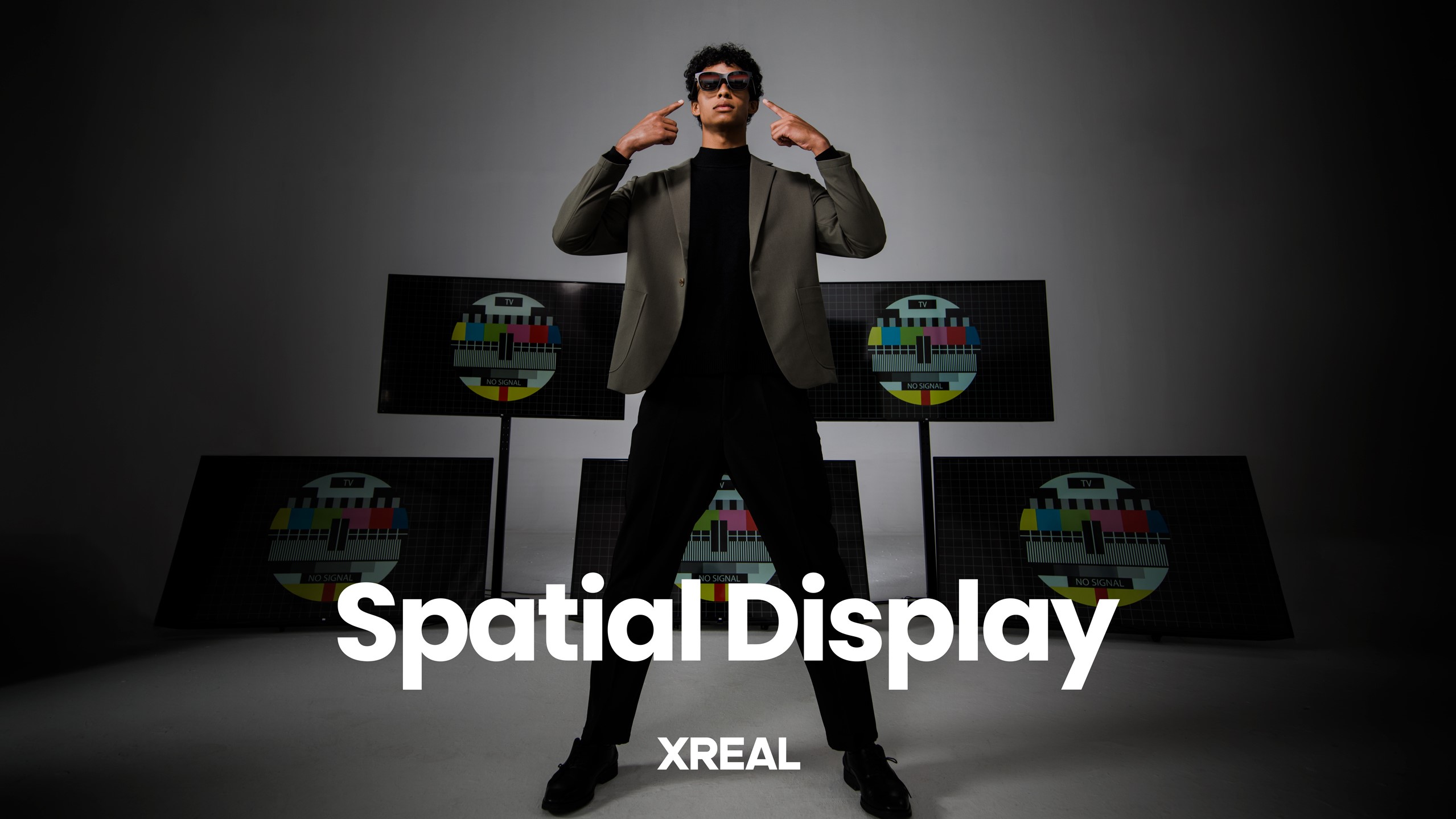 A person points at the Xreal Air glasses they're wearing, multiple displays are behind them, the words "Spatial Display" are in front of them