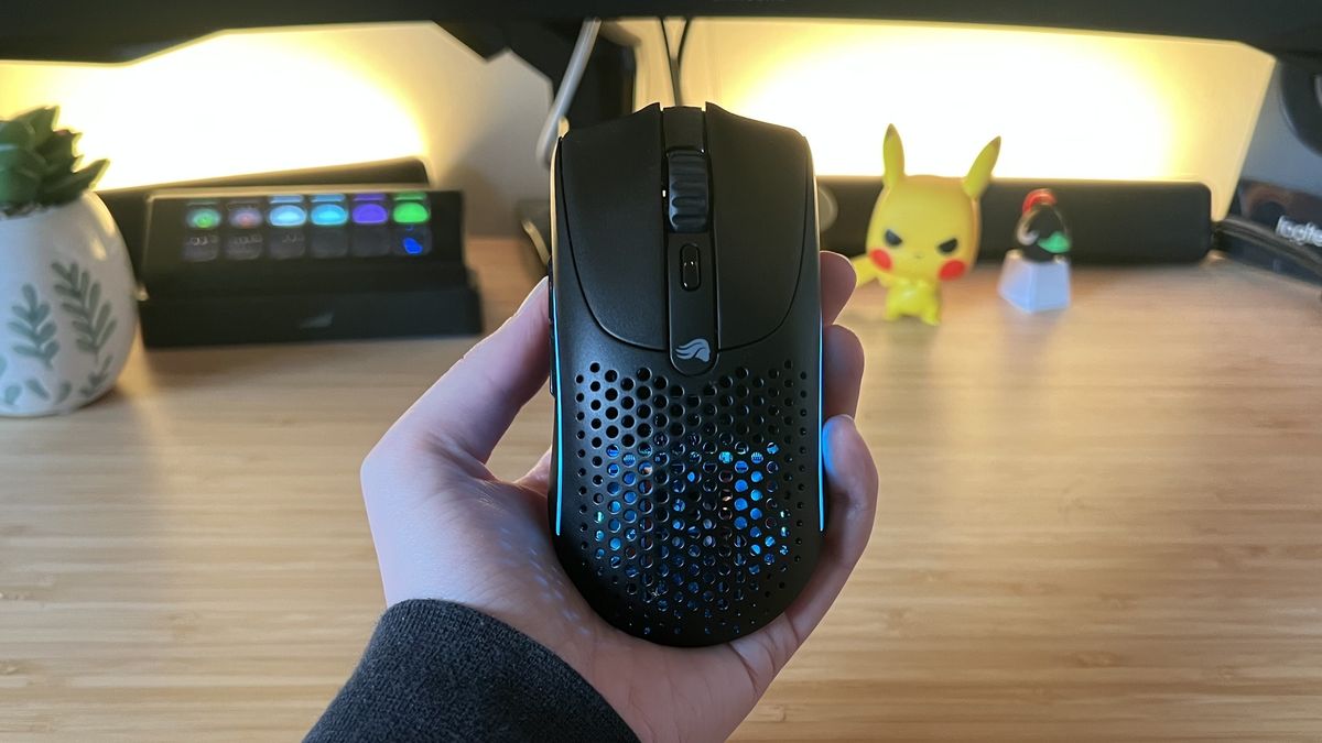 Hand holding Glorious Model O 2 Mini Wireless gaming mouse against a PC setup