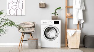 A laundry room with a washing machine, laundry hamper, chair, plant and shelves