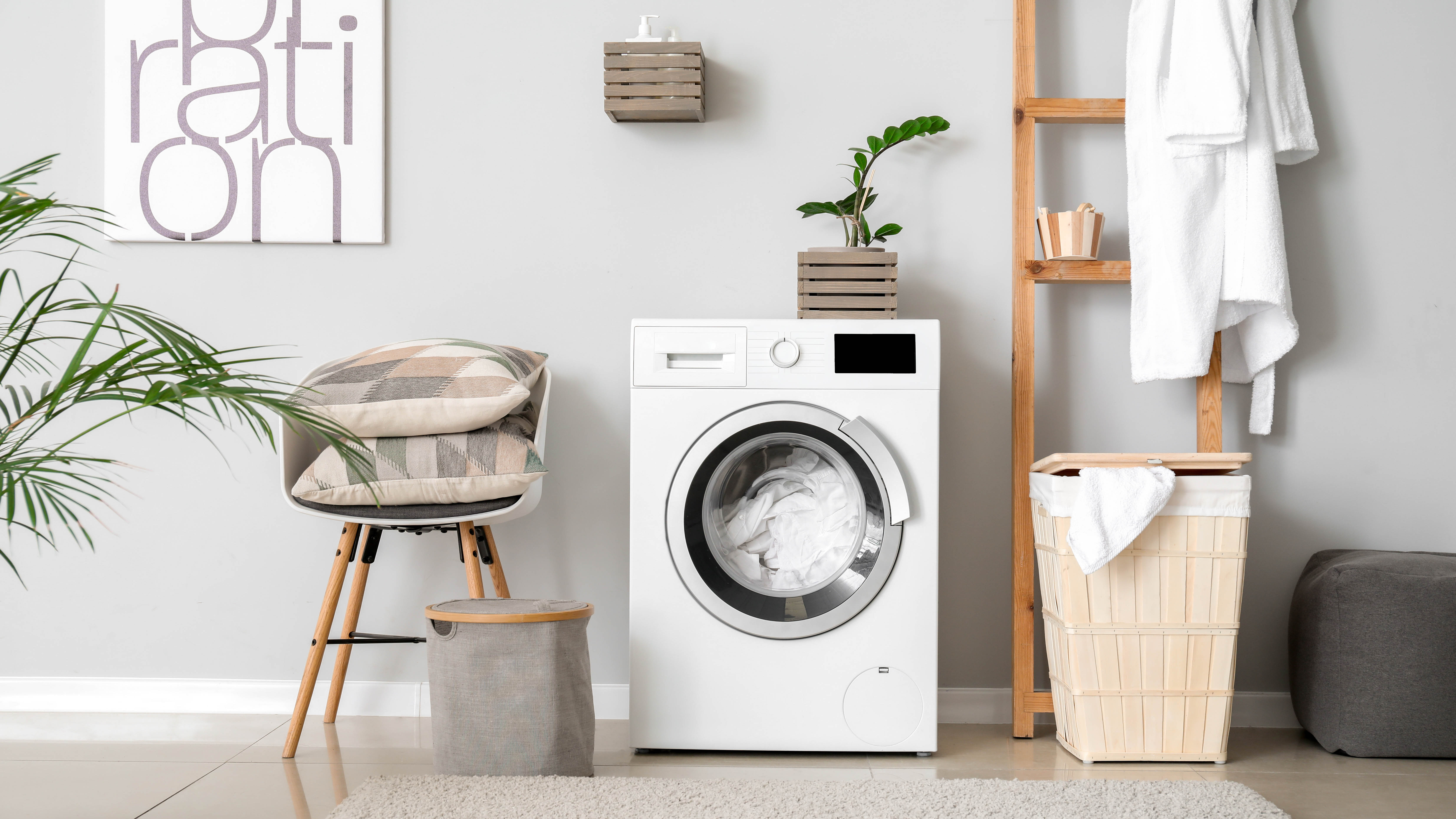 A laundry room with washing machine, laundry basket, chair, plant and shelves