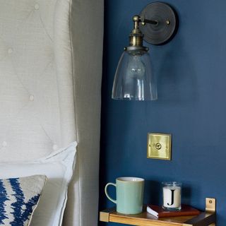 Glass shaded bedside wall light in blue bedroom