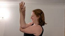Kat Bayly perform eagle arms, crossing her right elbow over her left and clasping the base of her right thumb with her left hand.