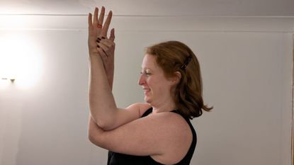 Kat Bayly perform eagle arms, crossing her right elbow over her left and clasping the base of her right thumb with her left hand.