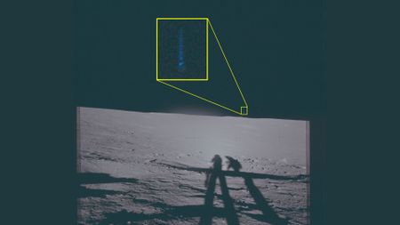 A black and white photo taken on the moon with two shadows of astronauts seen across the gray surface. In the dark sky a streak of blue light is surrounded by a yellow boxout.