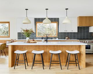 A kitchen with a white oak island and white quartz worktop, black and white bar stools and black backsplash tiling