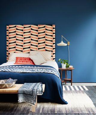 An example of guest room ideas showing a blue wall behind a bed with an orange and white headboard and white wall lamp