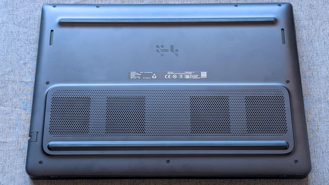 The underside of an Alienware laptop rests on a fabric surface, showing ventilation grilles, rubber feet, and a central label with certification markings and a QR code.
