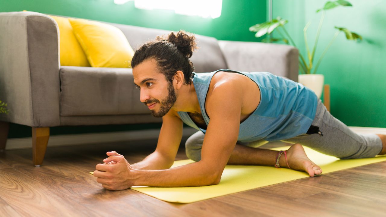 Man practices the pigeon pose in a home yoga session