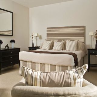 bedroom with neutral colour wall and mirror and chest and armchair