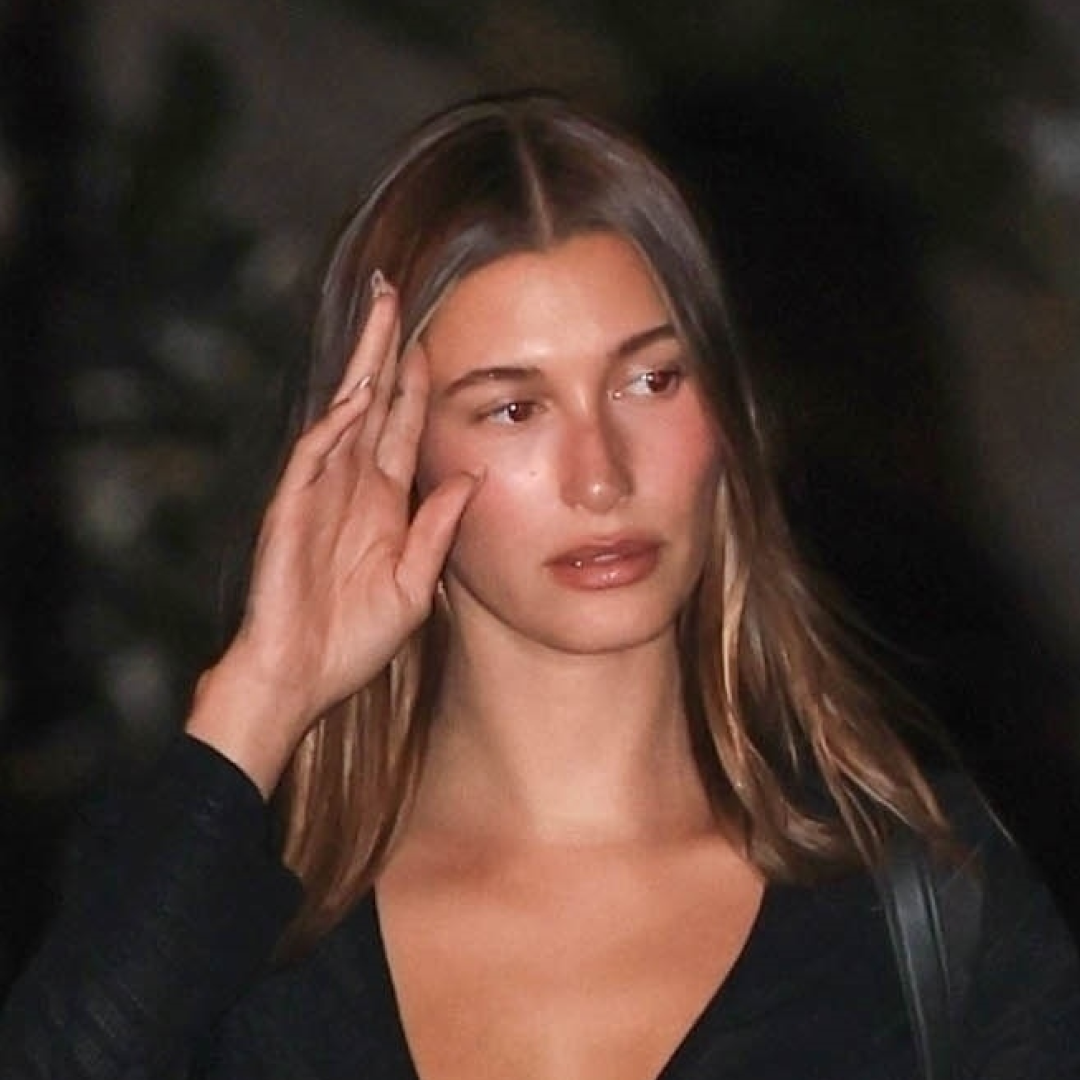Hailey Bieber wears black peep-toe sandals, a black lace-up top, and black pants