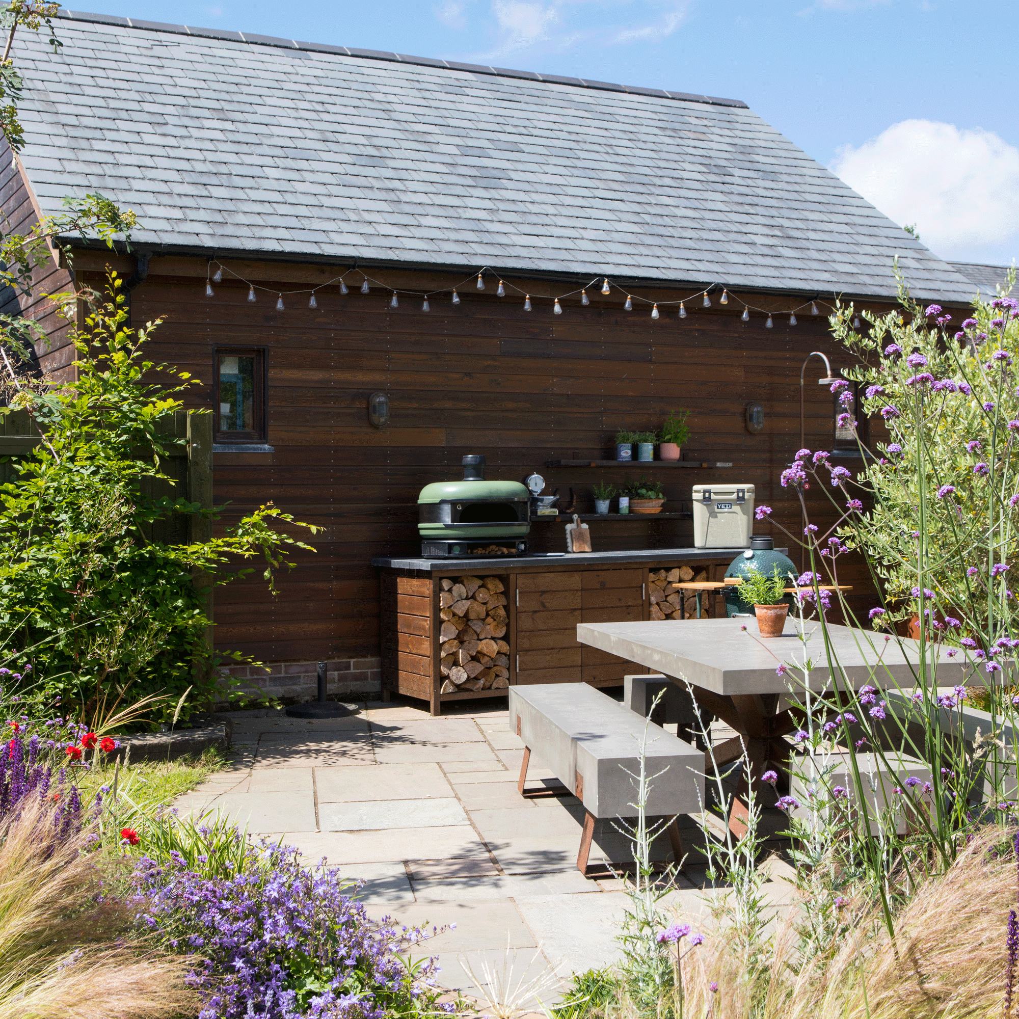 a patio with an outdoor kitchen area with a Gozney Dome pizza oven and a concretetopped table and bench set