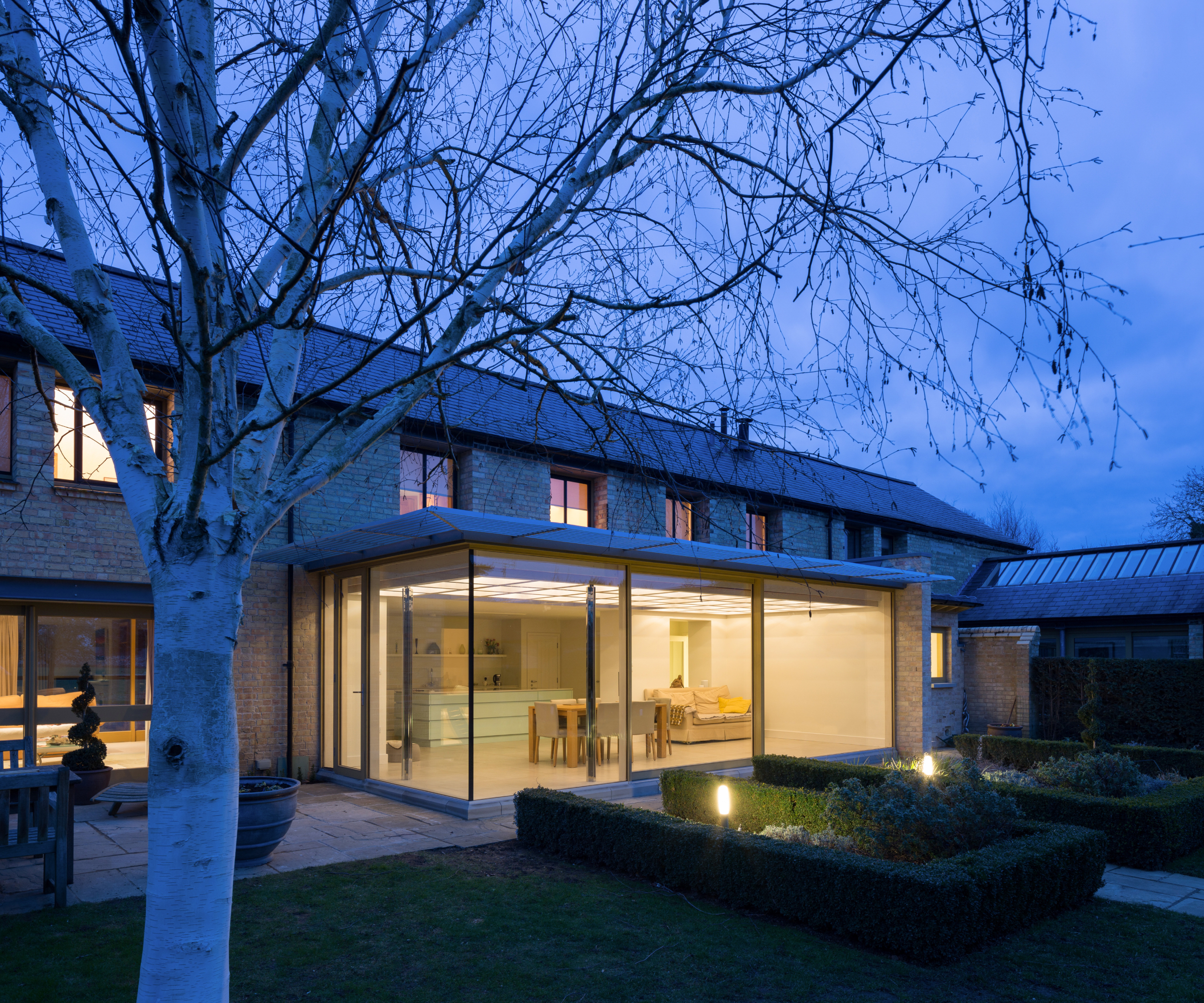 nighttime shot of single storey extension with glass corner and doors, metal grilled roof
