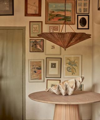 artwork hung all the way up the wall with a round wooden table and large rattan pendant