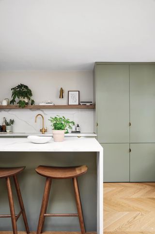 Kitchen with large white kitchen island, wooden flooring, green cupboard and wooden floor.