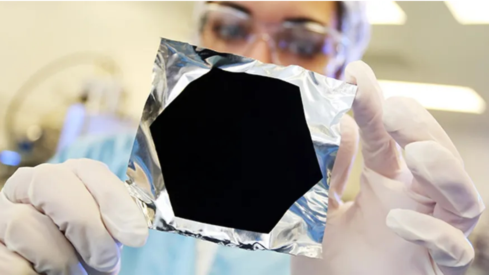 A photo of a scientist holding up a piece of foil covered in ultra-black paint