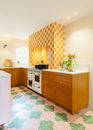 Pink and green tiled floor, with yellow and white checkerboard backsplash alcove and mustard yellow cabinetry