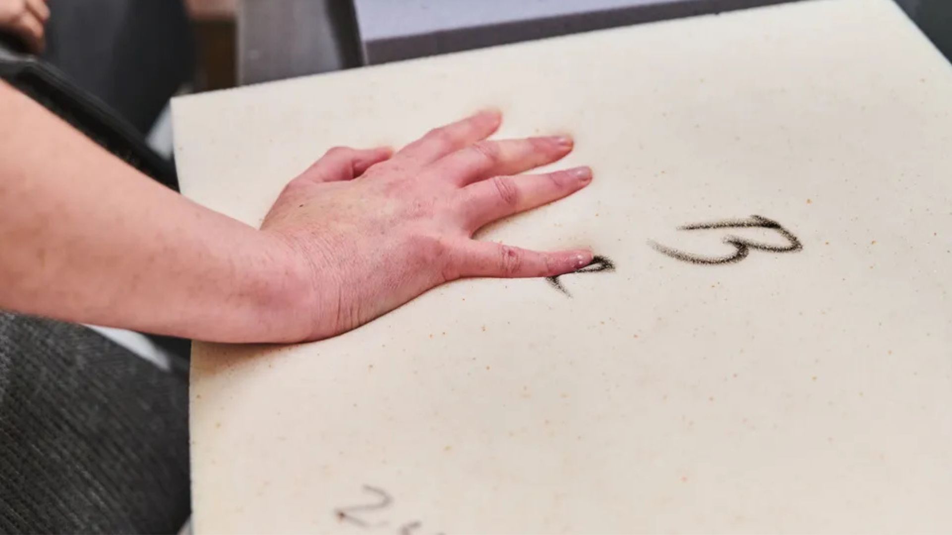 A hand feels a sample of memory foam infused with cooling copper gel in a factory.