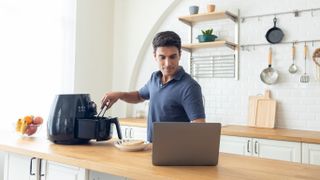 man using air fryer while looking at laptop