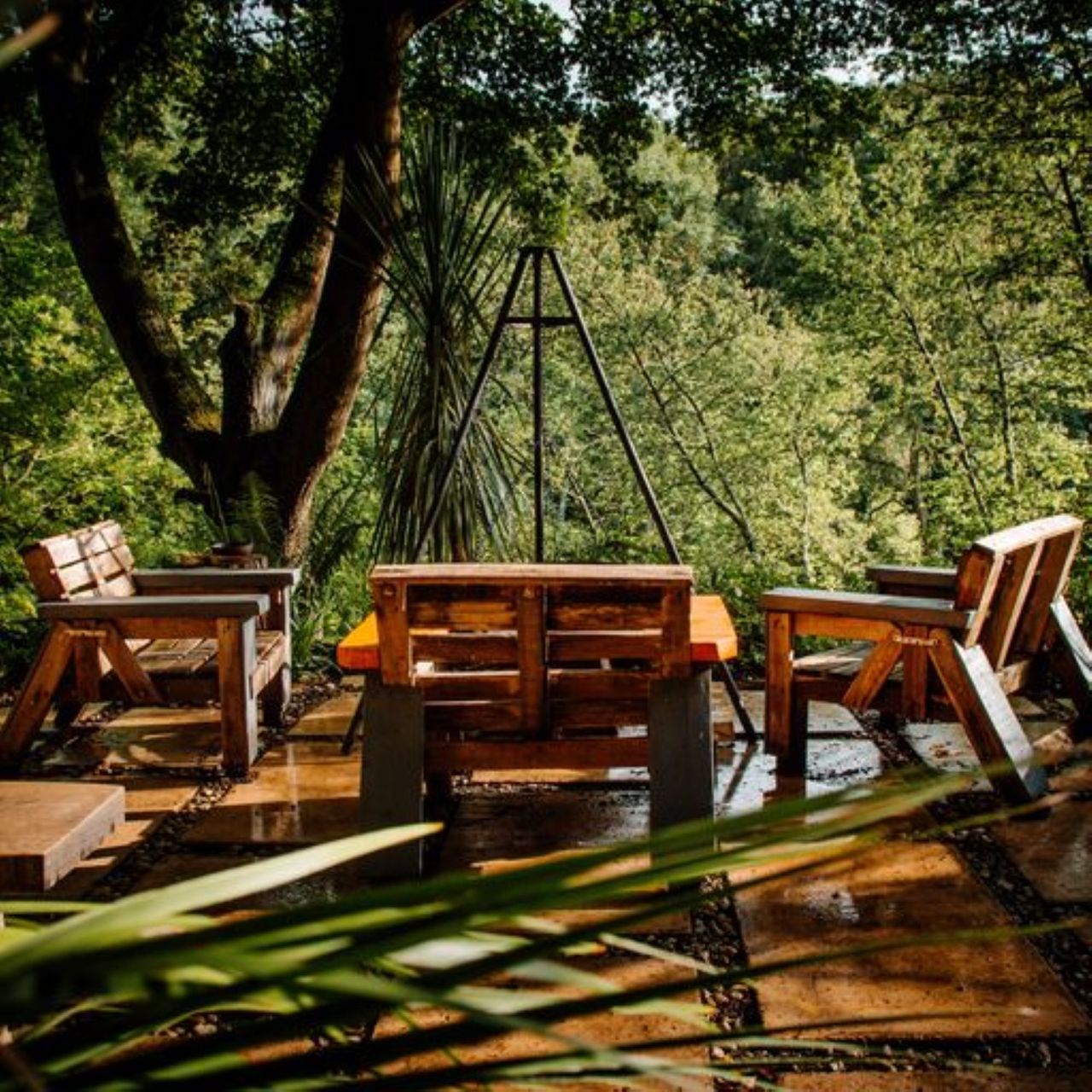 The outdoor sitting area includes 4 chairs surrounding the cooking area which overlooks the surrounding forestry landscape with a firepit in the middle