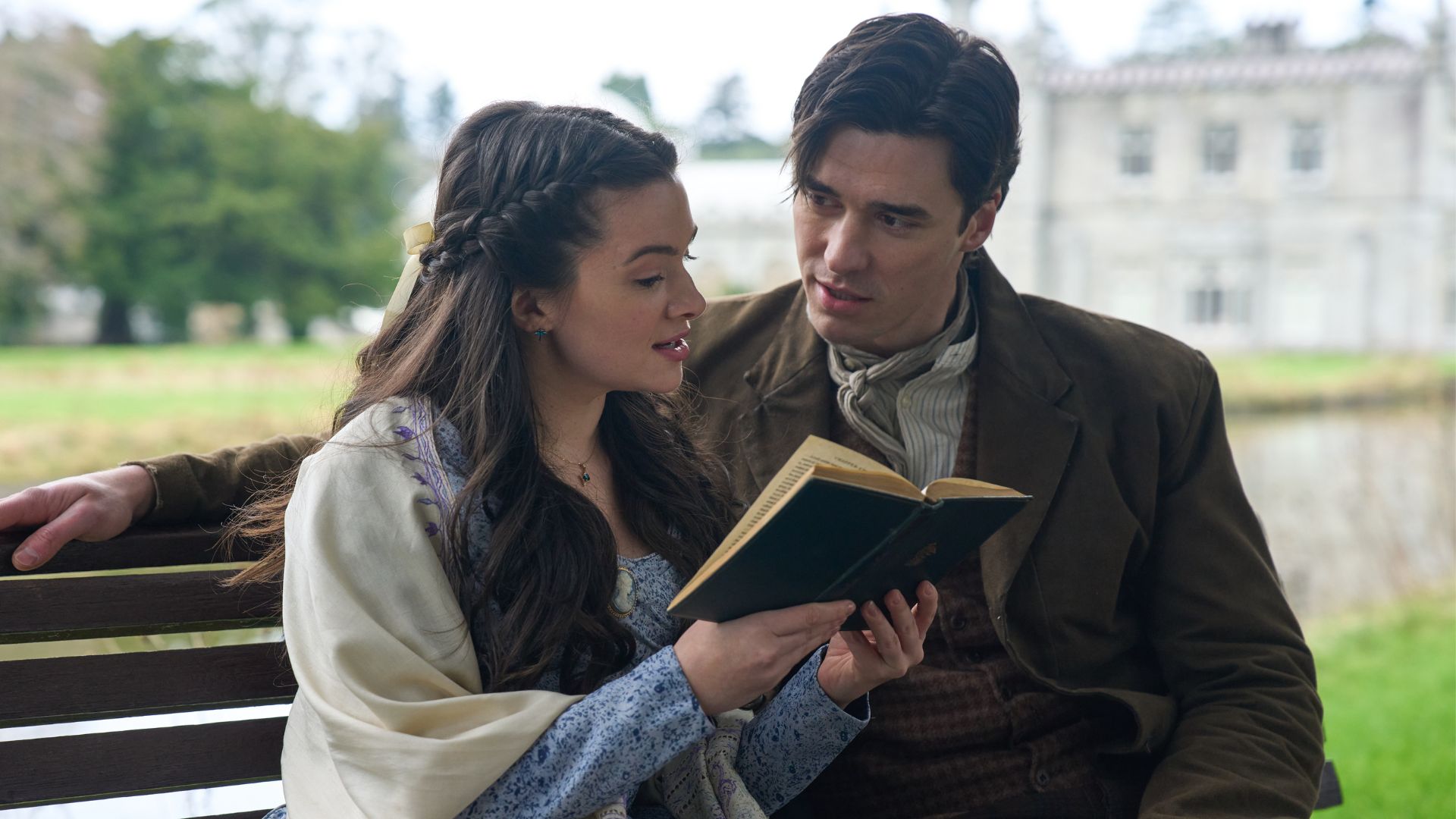 Cora reads to Liam on a bench outside a castle