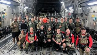 a group of about 25 military paratroopers poses for a photo in the cargo bay of their plane