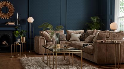 Sofology设计的深蓝色客厅角落，带有金色圆形镜子、棕榈树、壁炉和装饰艺术风格的家具