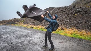 Man holding his rain poncho against strong wind in Iceland