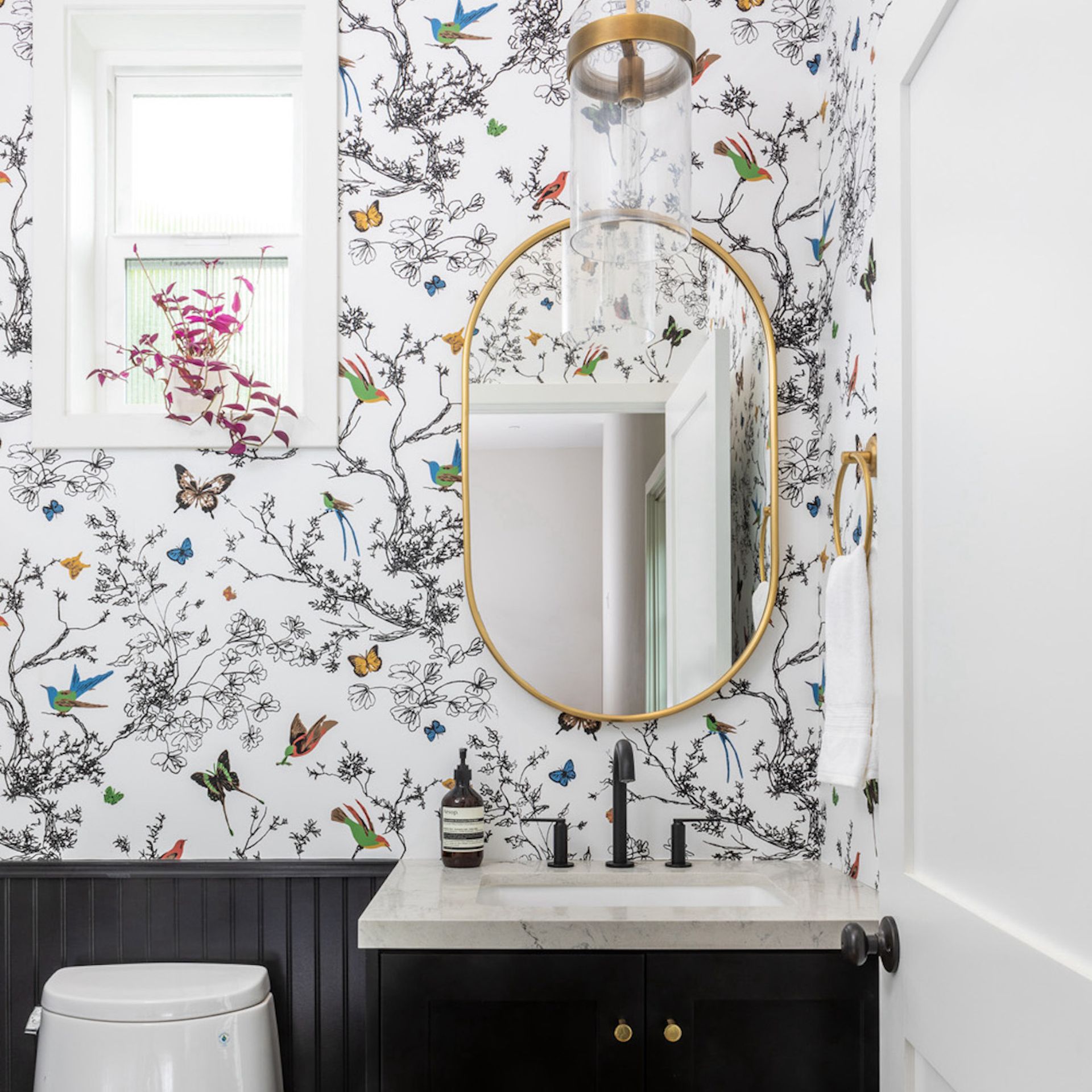 Kamar mandi dengan meja rias, dinding wallpaper, dan cermin berbingkai emas