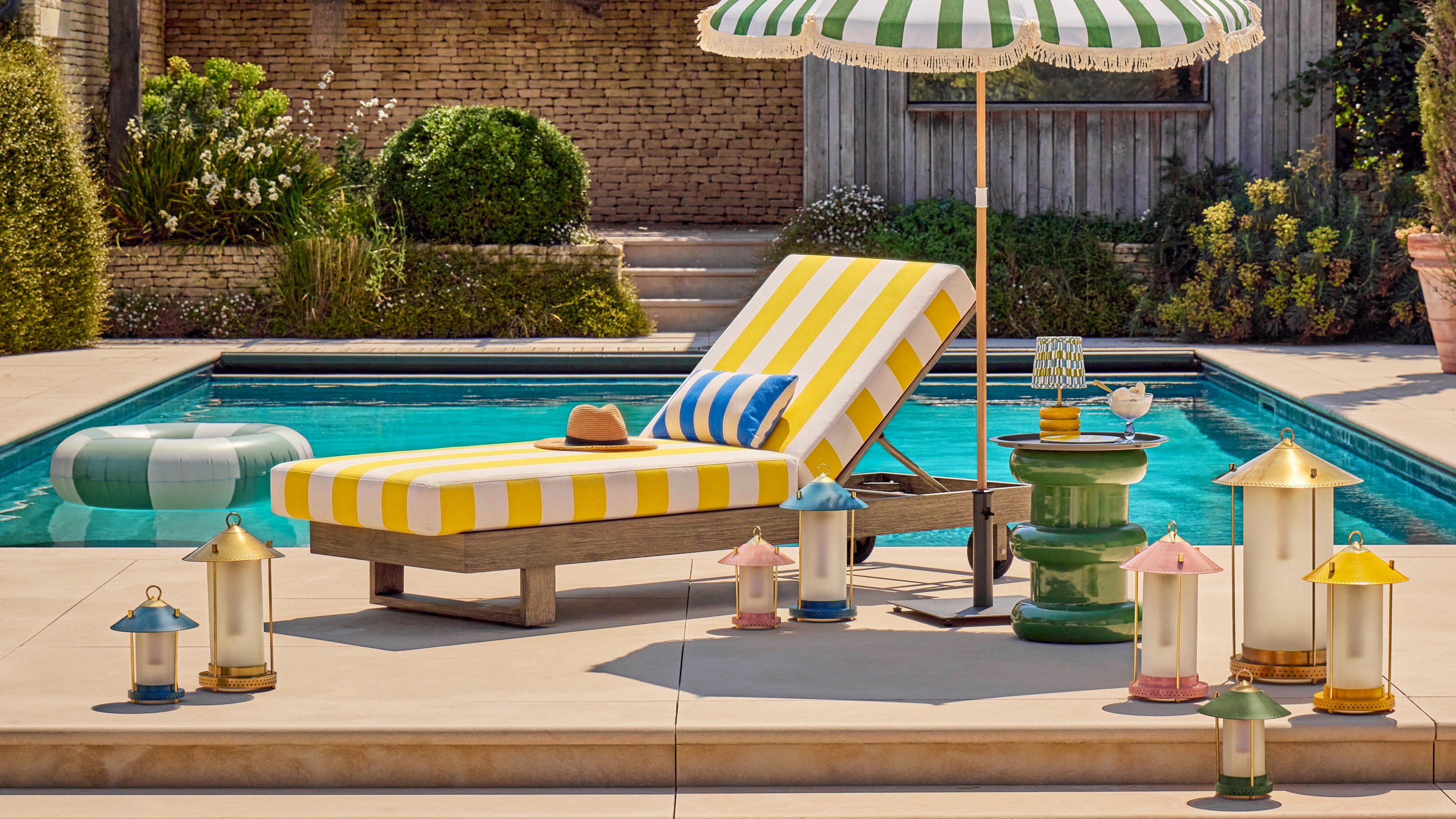 The Pooky Stefan lanterns by The Novogratz surrounding a yellow striped sun lounger next to a swimming pool