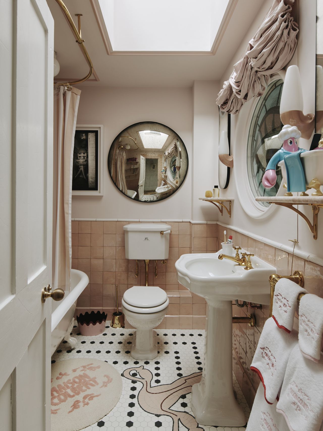 White and salmon pink coloured bathroom with a circular concave mirror and custom floor tiling with a uterus pattern.