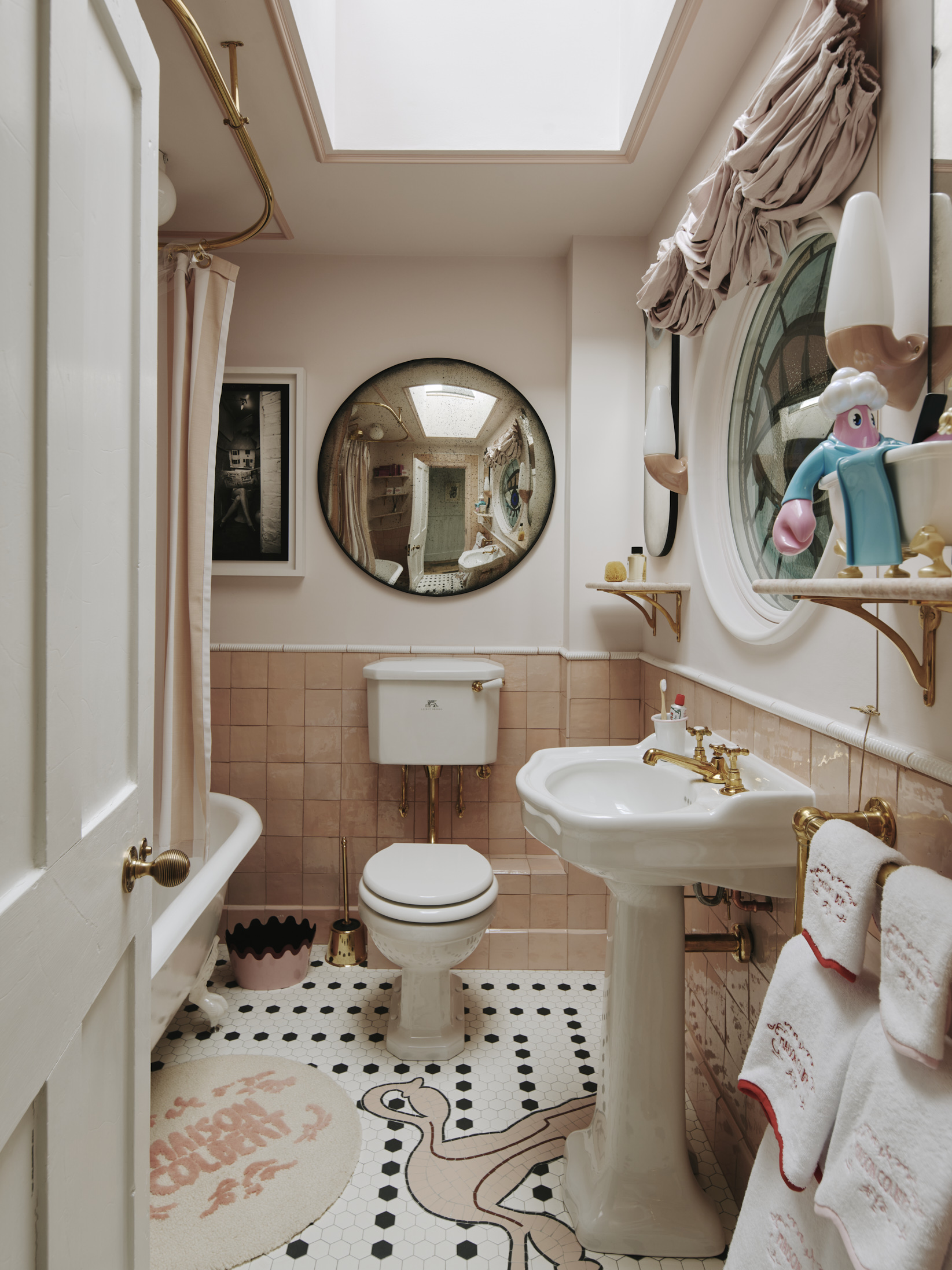 White and salmon pink coloured bathroom with a circular concave mirror and custom floor tiling with a uterus pattern.