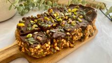 Cereal bar topped with chocolate, nuts and seeds on a wooden board
