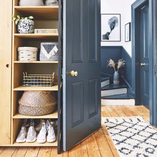 living room with open shelving with baskets, shoes, vases, rug, view to stairs, blue door and woodwork