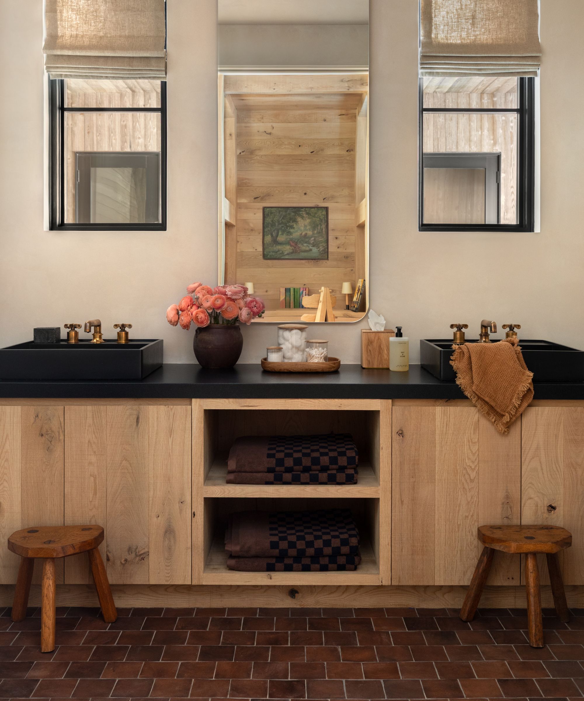 a neutral warm guest bathroom with two small windows, white oak vanity with dark counters and terracotta floor tiles